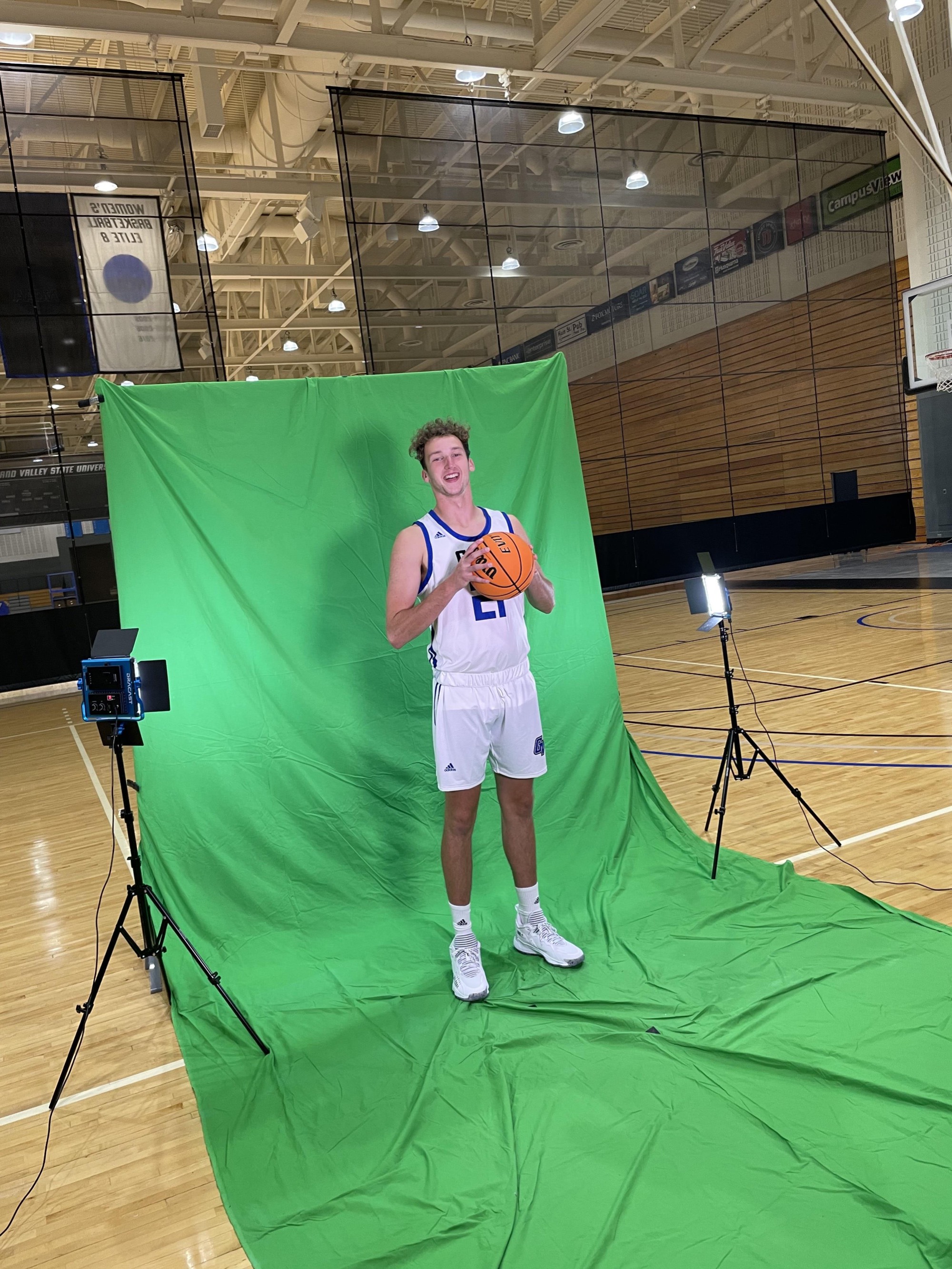 Men's basketball player wearing a white uniform holding a basketball posing on media day